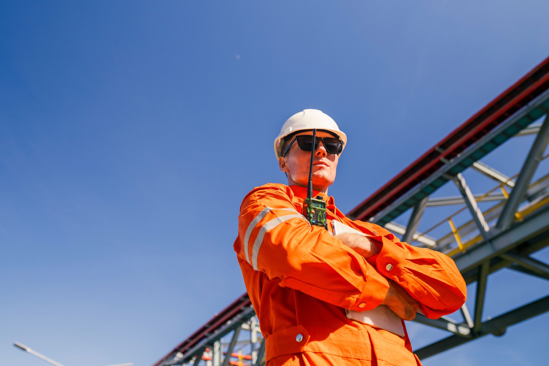 A professional engineer in protective gear, including a hard hat and orange coveralls, inspects a large industrial facility. The image highlights the importance of safety and expertise in the engineering field.