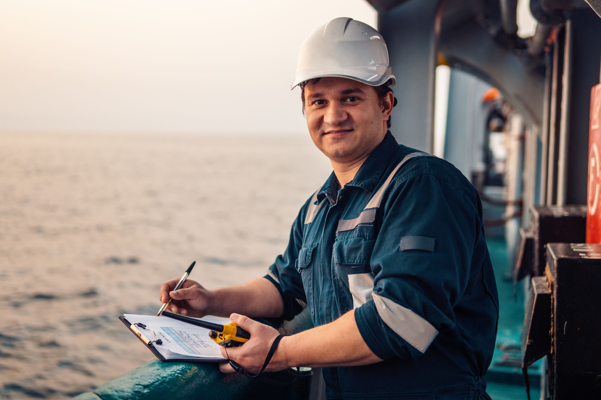 Deck Officer on deck of offshore vessel or ship , wearing PPE personal protective equipment. He fills checklist. Paperwork at sea